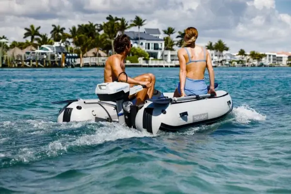 Two people riding in an inflatable motorboat with an electric outboard motor near the coastline.