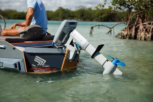 A person sits in a small boat powered by the Navy 6.0 Evo electric motor, gliding through shallow, clear water near mangroves under a partly cloudy sky. The partially submerged propeller ensures silent efficiency. Oceans EV