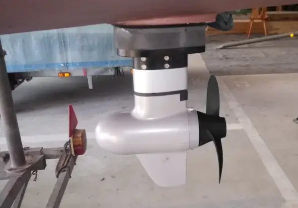 A boat's ePropulsion electric pod motor is mounted on the underside, featuring a streamlined design with a metallic body and a black propeller. The background shows part of a trailer and a parking area. Oceans EV
